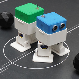 2 petits robots articulés avec une balle sur le rond central d'un mini terrain de foot