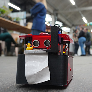 robot sur roues qui se balade dans les allées du salon avec un tout petit canard en plastique jaune